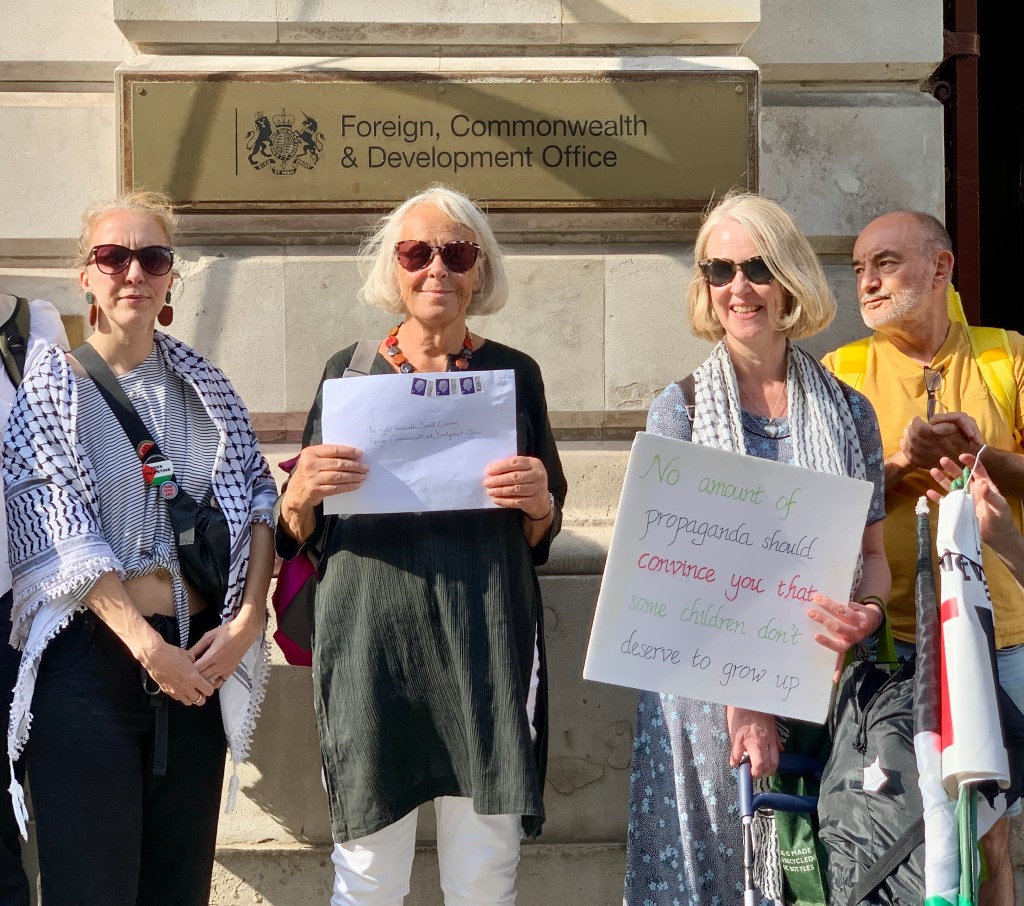 A group of four people holding signs and documents in front of the Foreign, Commonwealth & Development Office, advocating for children's rights.