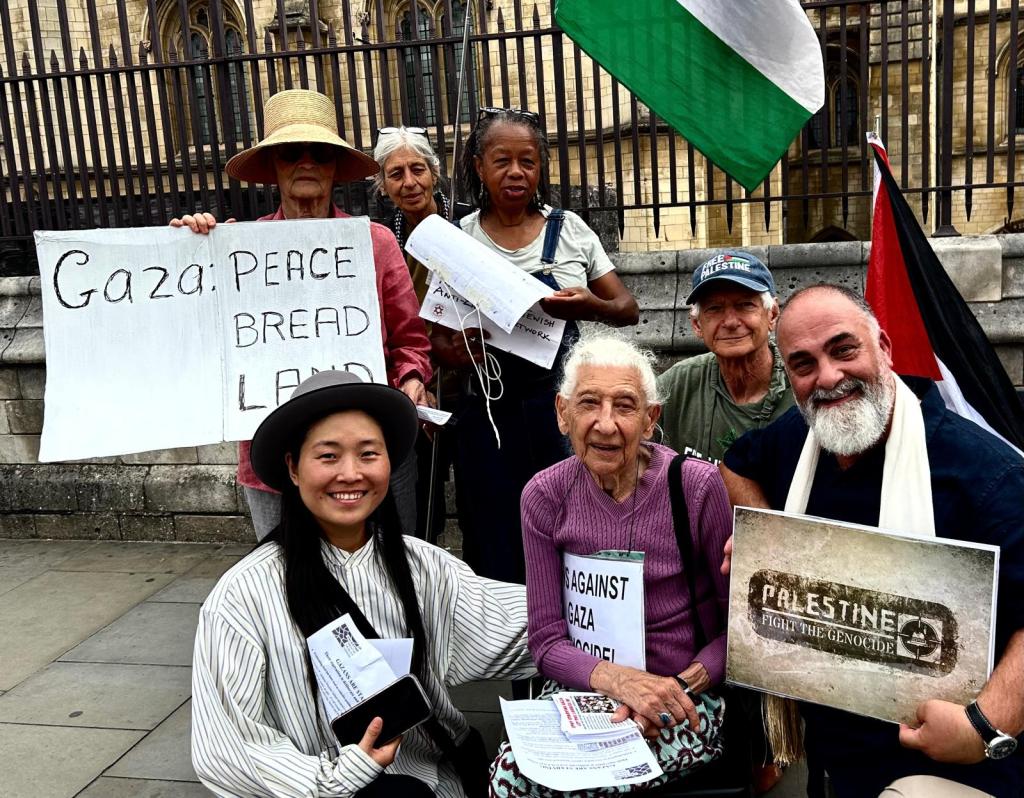 Group of supporters holding signs advocating for Gaza, including messages like 'Gaza: Peace Bread Land' and 'Against Gaza Genocide', with flags in the background.
